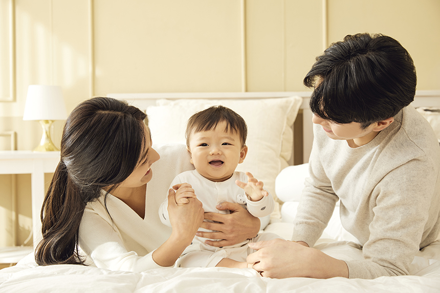 영유아를 바라보고 있는 침대위 부부의 모습