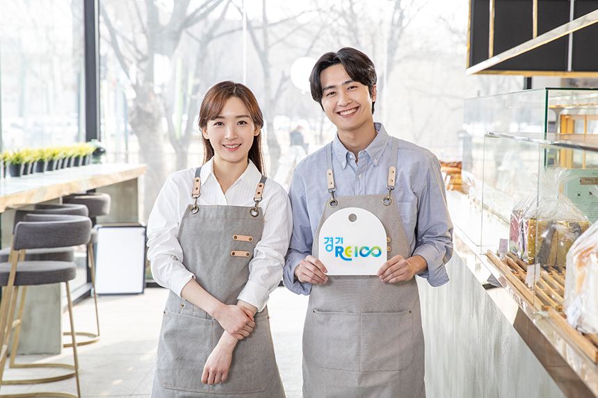 가게를 배경으로 경기RE100 팻말을 손에 든 두 소상공인 남녀의 모습