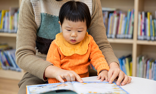 선생님의 품에 안겨 책을 읽는 영유아