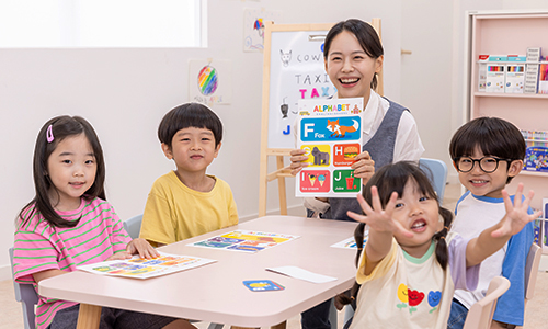 원실안의 탁자에 마주보고 앉은 유치원 선생님과 아동들이 화면을 바라보고 있다.