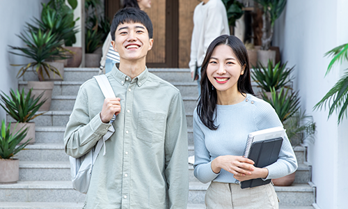 기숙사 계단 앞에서 환하게 웃고 있는 대학생 남녀