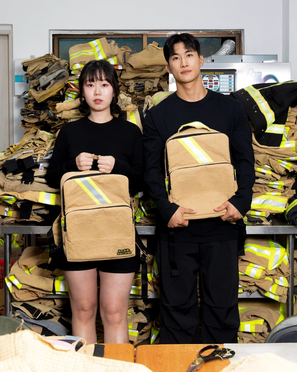 백팩 샘플 이미지:수거된 폐방화복을 배경으로 백팩을 들고 있는 두 남녀