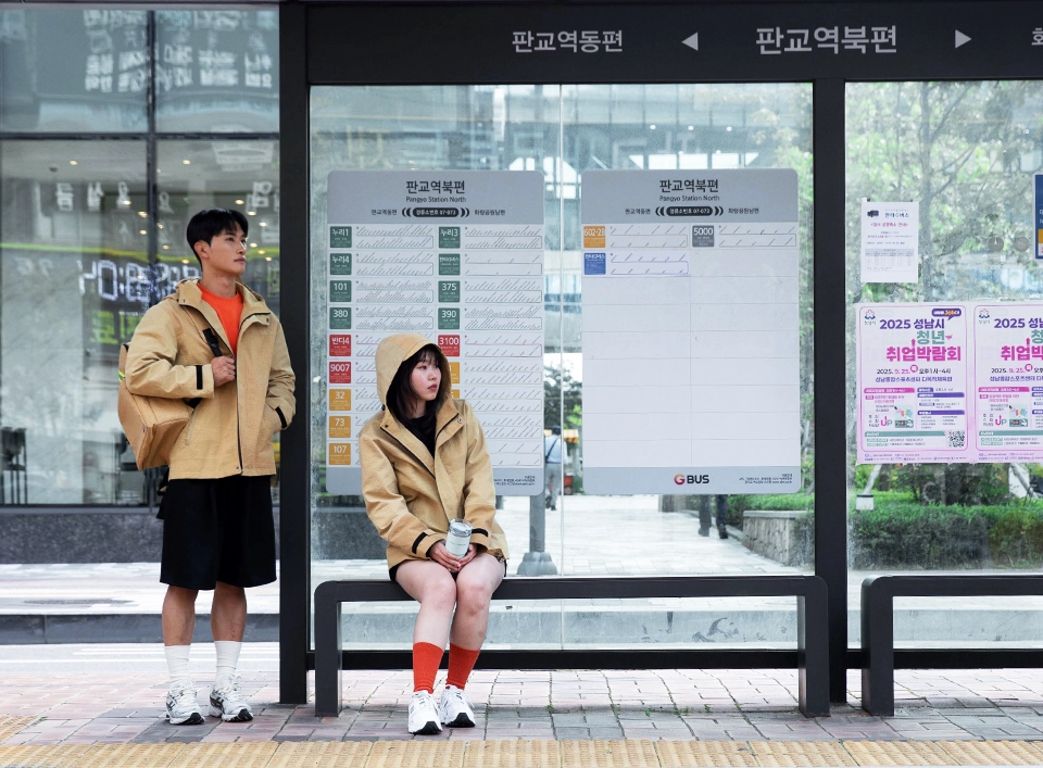 자켓과 백팩을 착용하고 버스를 기다리는 두 남녀