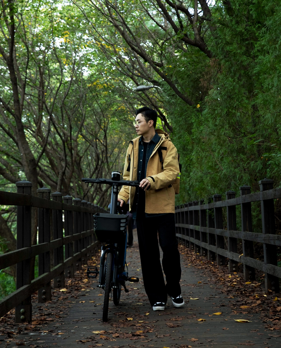 자켓과 백팩을 착용한 남성이 자전거를 끌고 산림 속 다리위에 서있는 모습 전신