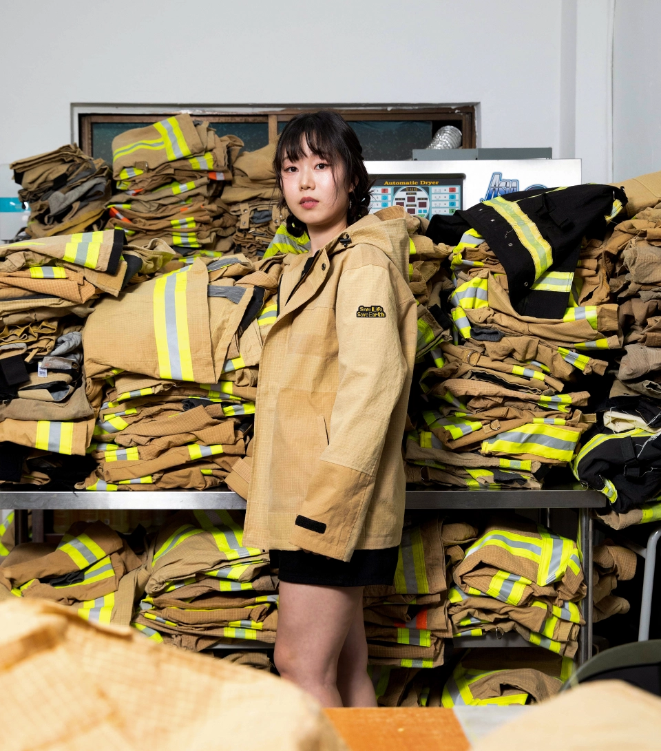 자켓 샘플 이미지: 쌓인 폐방화복 앞에 자켓을 입고 포즈를 취한 여성